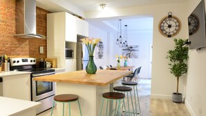 A modern kitchen with a wooden island, bar stools, and a brick wall. - FALL & WINTER SPECIAL! Huge Ground Floor apt with Courtyard - 5 bed + 6 bath (Montréal)