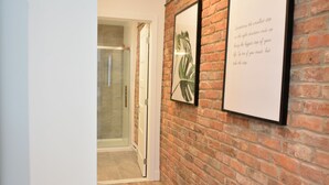 A hallway with a brick wall, a framed quote, and a glass door leading to a shower area. - FALL & WINTER SPECIAL! Huge Ground Floor apt with Courtyard - 5 bed + 6 bath (Montréal)