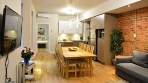 Eine moderne Küche mit Holzausstattung, ein Essbereich mit Holztisch und -stühlen sowie ein graues Sofa in einem Wohnzimmer.