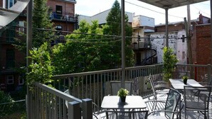Ein überdachter Außenbereich mit Tischen und Stühlen, umgeben von einem Holzzaun und Gebäuden im Hintergrund.