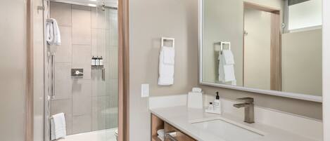 A modern bathroom with a glass shower enclosure, a large mirror, and a white countertop.