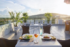 A rooftop terrace with a table set for two, two plates of food, a cocktail, and a tall glass of a blue beverage. - Nghi Lan Hotel (Phu Quoc)