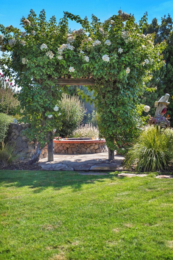 A garden with a pergola covered in white flowers, a stone wall, and a statue. - 3 bedroom, 2 bath, pool, new hot tub, outdoor kitchen, bar and lounge, fire pit (Sonoma)