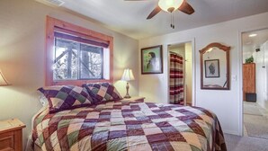 A bedroom with a large bed, a ceiling fan, a window with a view, and a door leading to another room.