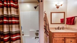 A bathroom with a white bathtub, wooden vanity with two sinks, a mirror, and a striped shower curtain.