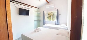 Quarto com cama, televisão na parede, janela com cortinas e prateleira fixada na parede.