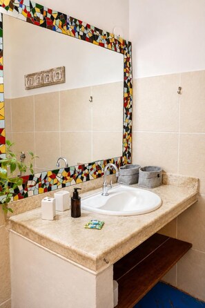 Casa de banho com painel de azulejos decorativos, uma pia branca, espelho e uma planta.