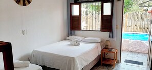 A single bed with white linens, a bedside table with a lamp, and a view of a swimming pool through an open door.