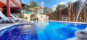 Piscina com cerca de madeira, espreguiçadeiras e mesa com guarda-sóis.