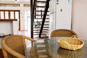 A dining area with wicker chairs, a glass table, and a wicker basket.