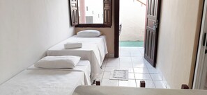 A narrow hallway with three beds aligned against the wall, a tiled floor, and a door leading outside. - Pousada Semente (Porto Seguro)