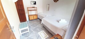 A hotel room with a bed, a small table with a chair, a TV, and a shelf unit. - Pousada Semente (Porto Seguro)