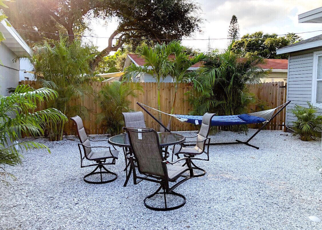 Une terrasse extérieure avec une table ronde et quatre chaises, entourée d’une clôture en bois et de différentes plantes.