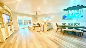 A spacious room with a wooden floor, a dining area with a table and chairs, a kitchen area with a counter and cabinets, and a large window providing natural light.