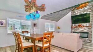 A dining area with a wooden table and chairs, a sofa, and a TV mounted on a stone wall.