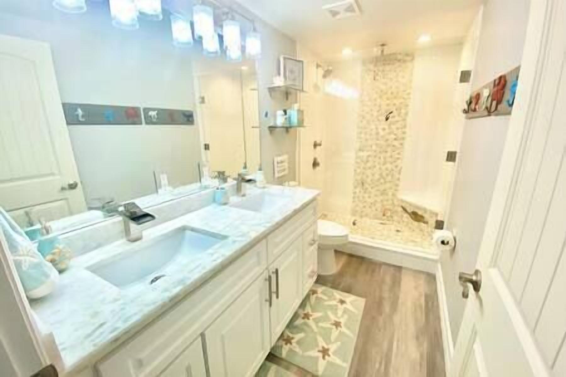 Une salle de bain moderne avec un grand meuble-lavabo, une douche dotée d’une porte en verre et des toilettes.