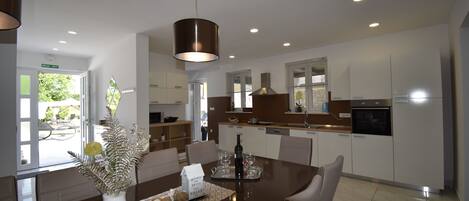 A modern kitchen with white cabinets, a central island, and a dining area with a vase of flowers.