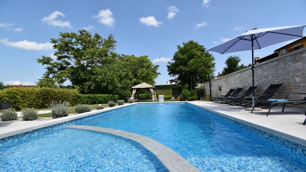 A swimming pool with a tiled edge, surrounded by lounge chairs and a pergola.