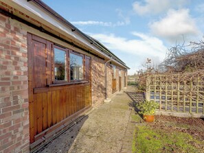 A brick building with wooden windows and a gravel path. - Lovely single-storey cottage with garden in a quiet rural location. (Hassocks)