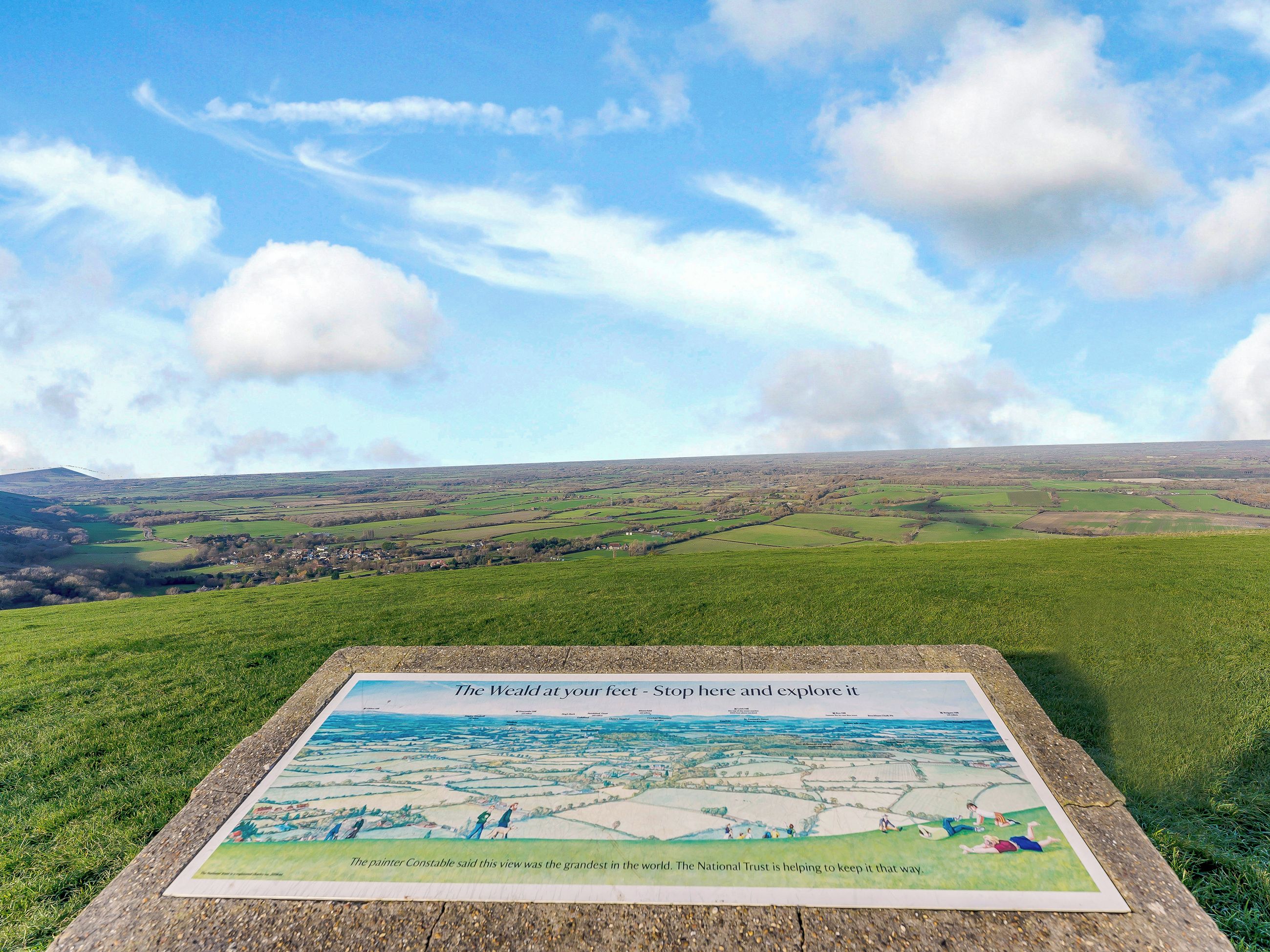 A scenic view of a countryside landscape with a signboard displaying a map and information about the Weald.