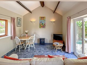 A dining area with a table and chairs, a television, and a window with curtains. - Lovely single-storey cottage with garden in a quiet rural location. (Hassocks)