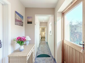 A hallway with a door, a window, a vase with flowers, and a lamp.