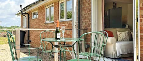A brick building with a patio area featuring green metal chairs and a table with a bottle and glass.