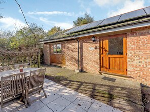 A brick building with a wooden door, a window, and a solar panel roof. - Lovely single-storey cottage with garden in a quiet rural location. (Hassocks)