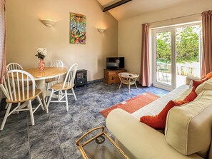 A living room with a sofa, dining table, chairs, a TV, and a sliding glass door to a balcony. - Lovely single-storey cottage with garden in a quiet rural location. (Hassocks)