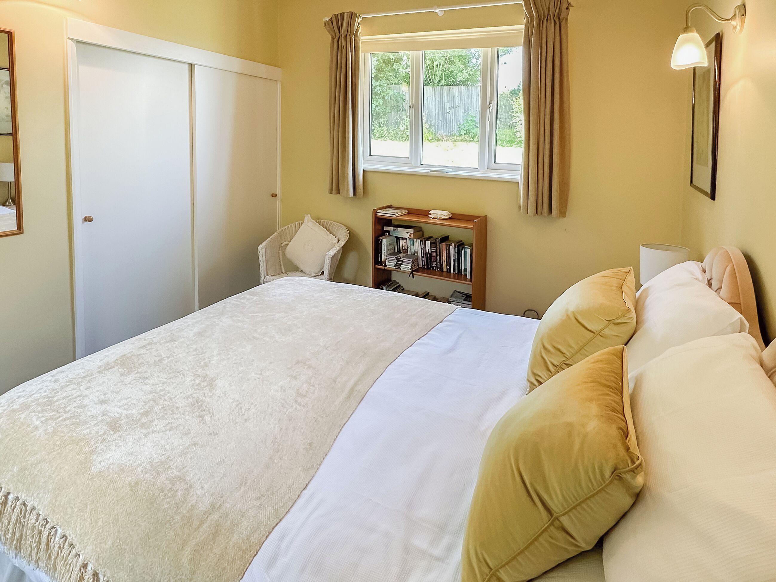 Un dormitorio con cama, una silla, una estantería y una ventana con cortinas.