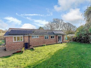 A brick house with solar panels on the roof, a front door, and a small front yard.