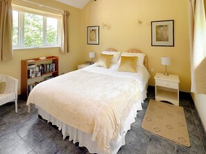 A neatly arranged bedroom with a large bed, bedside tables, a bookshelf, and a window with curtains.