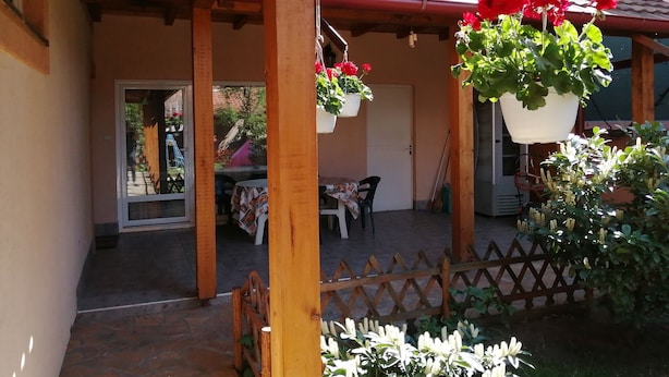 Un patio techado con macetas colgantes, cerca de madera y una mesa con sillas.