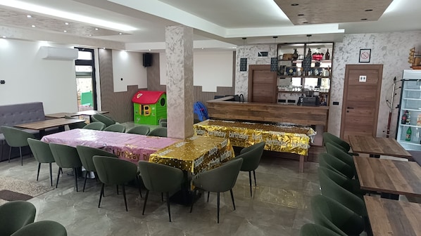 A restaurant with multiple tables, some covered with birthday-themed tablecloths, and a play area with a green house-like structure.