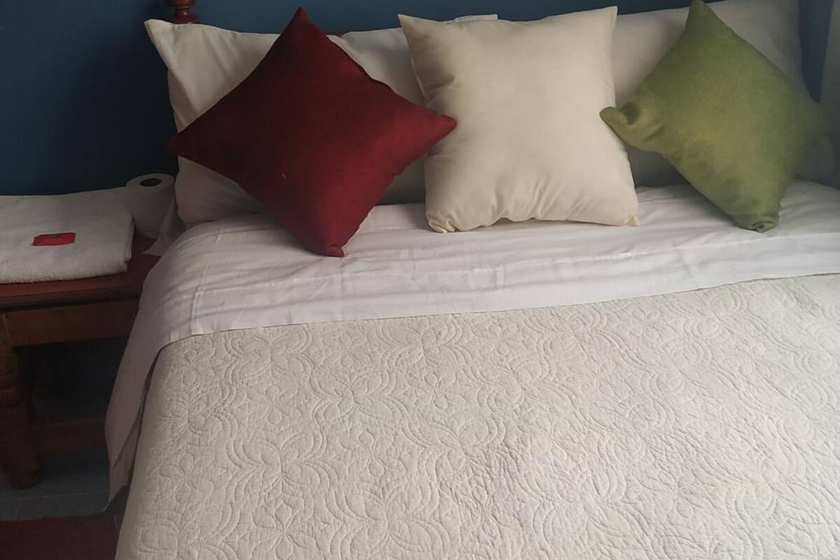Uma cama com colcha branca e três almofadas em vermelho, branco e verde.