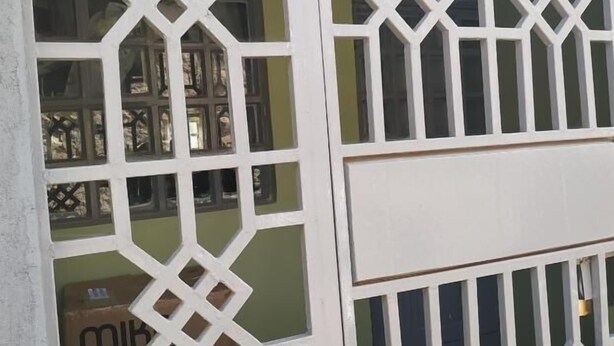 A white metal gate with geometric patterns and a red base. - The Rhine Guest House-Eldoret (Eldoret)