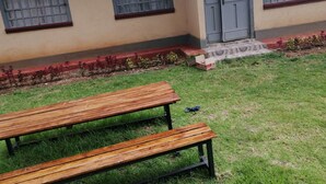 A wooden bench in a grassy area with a building in the background. - The Rhine Guest House-Eldoret (Eldoret)