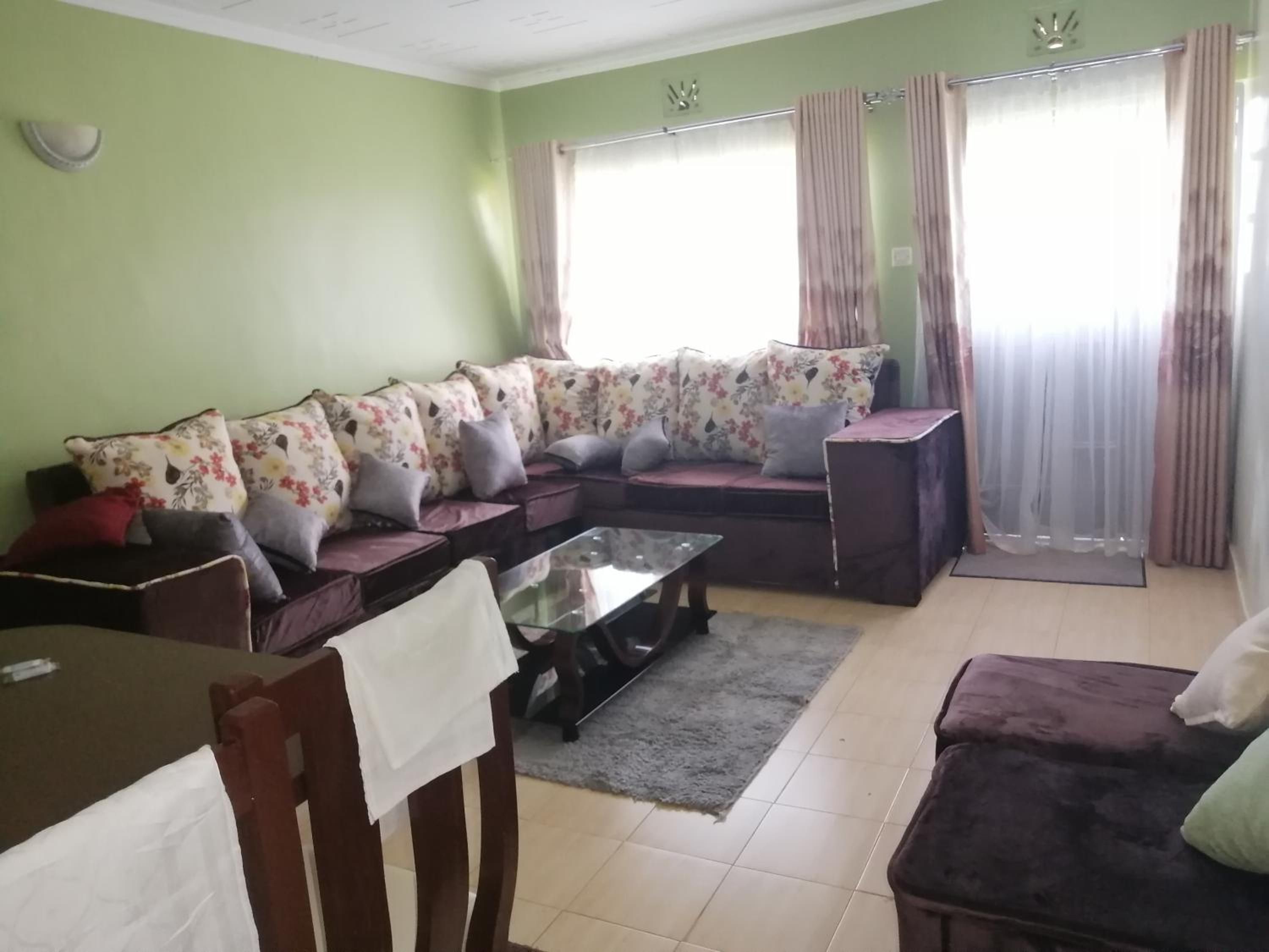 Una sala de estar con un sofá seccional, una mesa de centro de vidrio, una mesa de comedor con sillas y una pequeña mesita auxiliar.