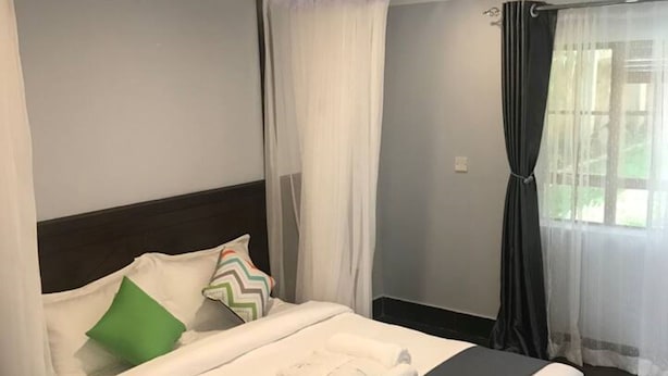 A modern hotel room with a large bed, white bedding, and a dark headboard. - Maryland Hotel Kisumu (Kisumu)