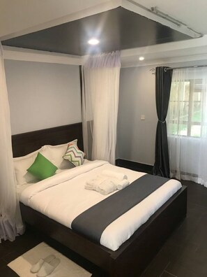 A modern hotel room with a large bed, white bedding, and a dark headboard. - Maryland Hotel Kisumu (Kisumu)