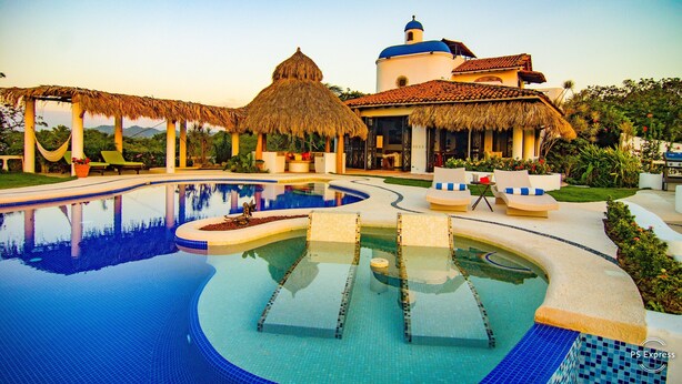 A resort with a swimming pool, thatched-roof structures, and a building with a blue dome.