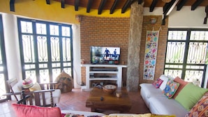 A living room with a brick wall, a television on a white stand, a sofa with colorful cushions, and a wooden coffee table.