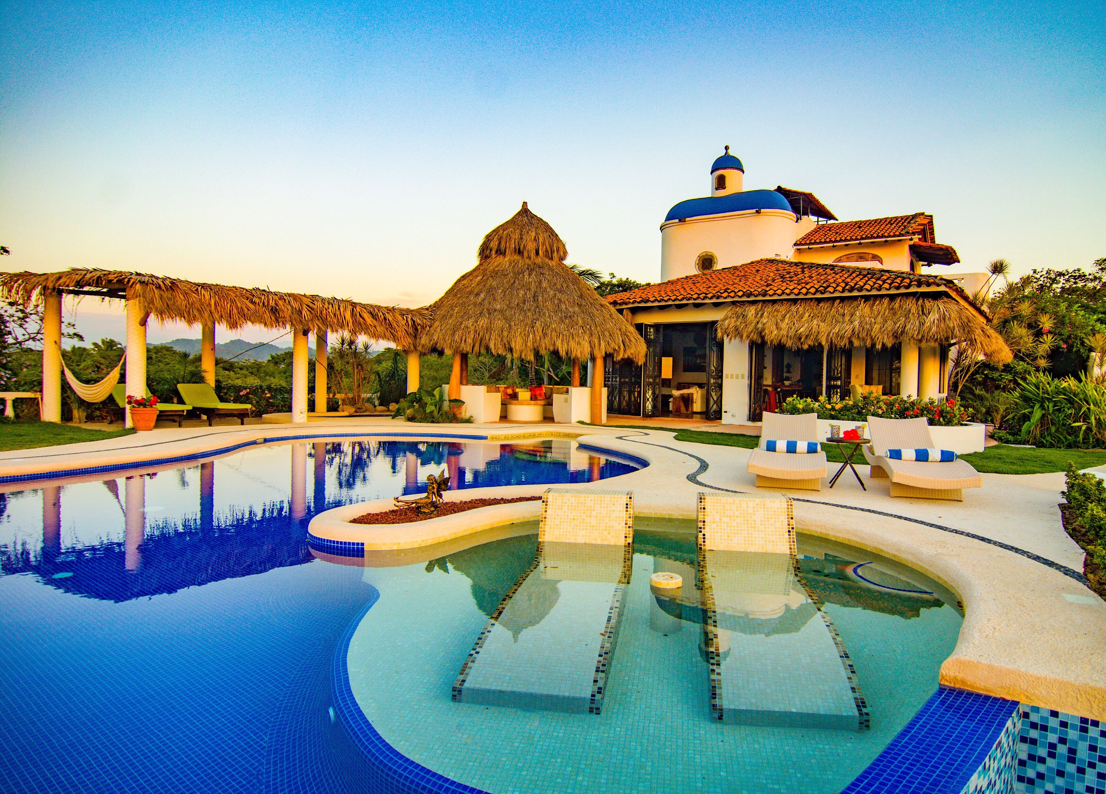 A resort with a swimming pool, thatched-roof structures, and a building with a blue dome.