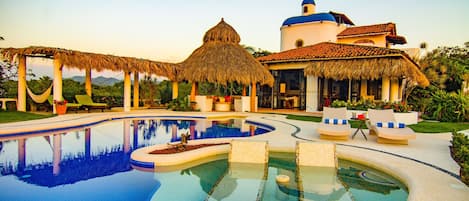 A resort with a swimming pool, thatched-roof structures, and a building with a blue dome.