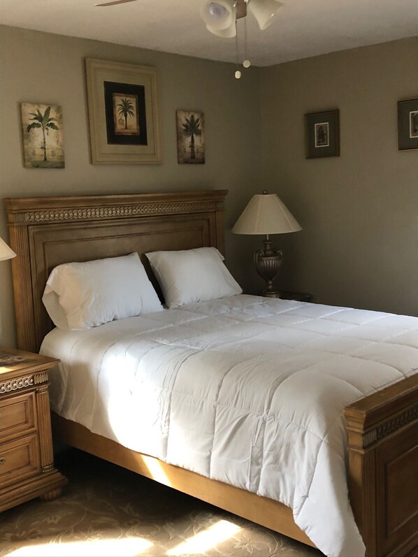 A neatly made bed with a wooden headboard, a bedside lamp, and framed artwork on the wall.