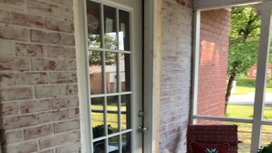 A covered porch with a brick wall, a sliding glass door, and two chairs with patterned cushions. - Cozy comfortable home near lakes, parks and downtown Sumter (Sumter)