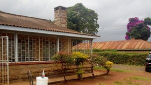 A house with a covered patio, a white chair, and a small table. - Banana Leaf Hotel (Nyeri)