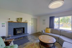 Sala de estar con chimenea, un sofá, una mesa redonda de centro y una ventana con vista a árboles.
