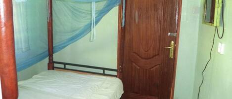 A single bed with a canopy, a wooden door, and a small table.