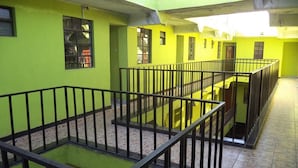 A multi-level corridor with yellow walls and black railings, featuring a central open space and multiple windows. - Millennium Guest House (Narok)